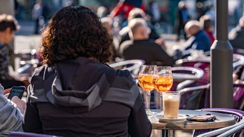 Besucher eines Straßencafes in der Innenstadt von Darmstadt im Sonnenschein, im Vordergrund eine Frau von hinten vor zwei Drinks und einem Kaffee