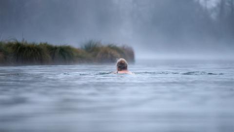 Frau schwimmt im Winter im See - Nebel steigt auf