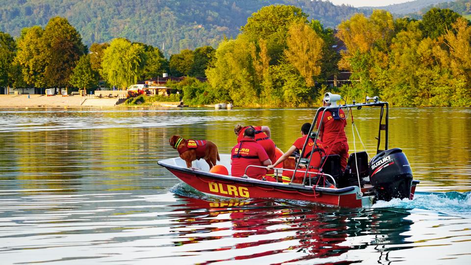 Einsatzkräfte in einem roten Schlauchboot fahren über einen Badesee.