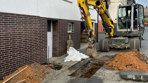 Bagger steht vor Loch mit Leitung