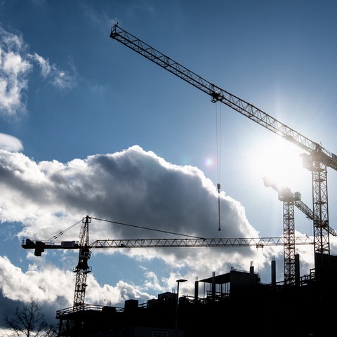 Hinter den Baukränen an einer Baustelle scheint die Sonne.