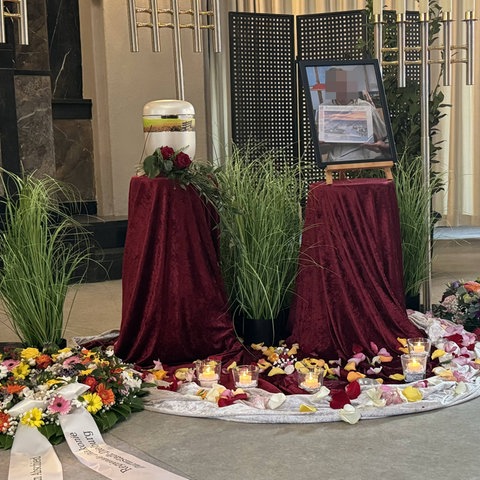 Blumen und Kränze liegen vor einer Urne in der Trauerhalle.