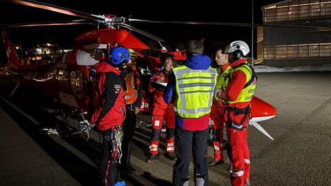 Retter der Bergwacht reden vor einem stehenden Helikopter miteinander. Alle haben rote Sachen an.