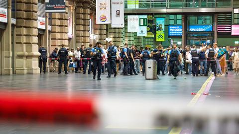 Frankfurter Hauptbahnhof: Zahlreiche Reisende hinter Absperrband in Abfahrthalle. Davor stehen bis zu zehn Polizisten.