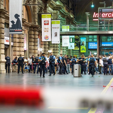 Frankfurter Hauptbahnhof: Zahlreiche Reisende hinter Absperrband in Abfahrthalle. Davor stehen bis zu zehn Polizisten.