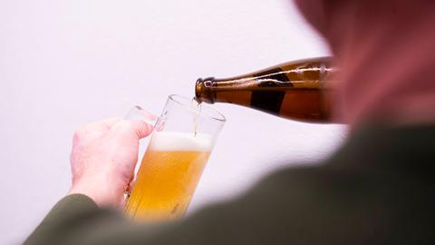 Eine Person gießt Bier aus einer Flasche in ein Glas