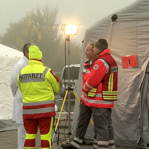 Mehrere Rettungssanitäter und Ärzte stehen vor großen weißen Zelten.