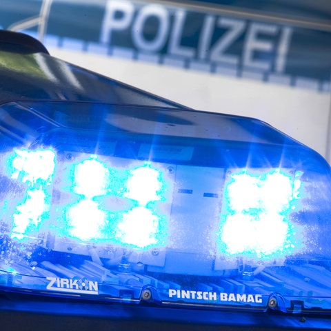 Nahaufnahme eines leuchtenden Blaulichts auf einem Autodach. Im Hintergrund unscharf der Schriftzug "Polizei" auf einem Auto.