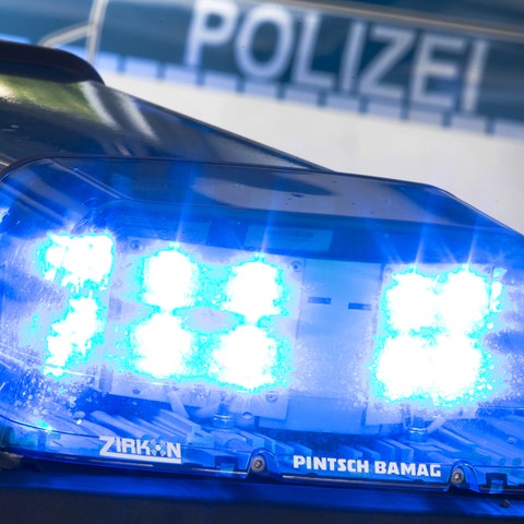 Nahaufnahme eines leuchtenden Blaulichts auf einem Autodach. Im Hintergrund unscharf der Schriftzug "Polizei" auf einem Auto.