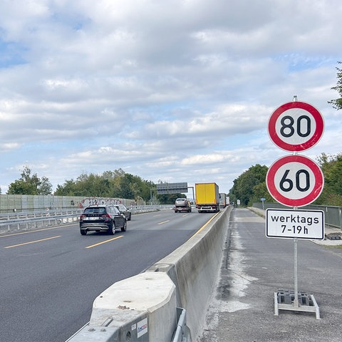 Foto: Blick auf eine Autobahn mit fahrenden Autos vom Seitenstreifen. Am rechten Rand stehen Geschwindigkeitsbegrenzungsschilder.