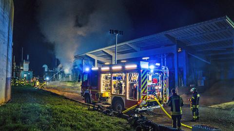 Feuerwehrleute löschen mit einem Schlauch einen brennenden Behälter