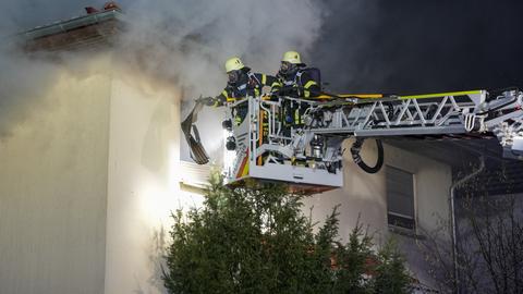 Wohnhausbrand in Büttelborn-Worfelden - aus dem Dach eines Wohnhauses schlagen Flammen - Feuerwehr mit Blaulicht und ausgefahrener Drehleiter löschen