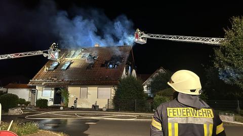 Löscharbeiten bei Brand in Eschwege - Rauch steigt aus dem Dach eines Wohnhauses empor - im Vordergrund ein Feuerwehrmann 