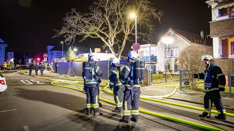 Feuerwehrleute vor einem Haus, wo Ruß an den Wänden oberhalb von zwei großen Kellerfenstern zu sehen ist