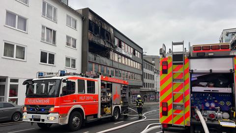 Das Bild zeigt eine Straße in der Kasseler Innenstadt. Ein Gebäude ist ausgebrannt, die Fassade schwarz. Davor stehen Löschfahrzeuge der Feuerwehr.