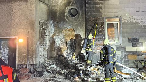 Zwei Feuerwehrleute im Einsatz in Kassel an der verkohlten Fassade eines dreistöckigen Wohngebäudes. 