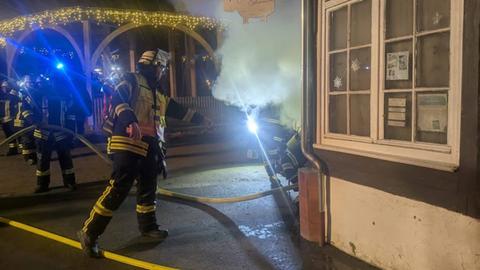 Feuerwehrleute stehen rund um einen kleinen Pavillon, aus dem Rauch drängt