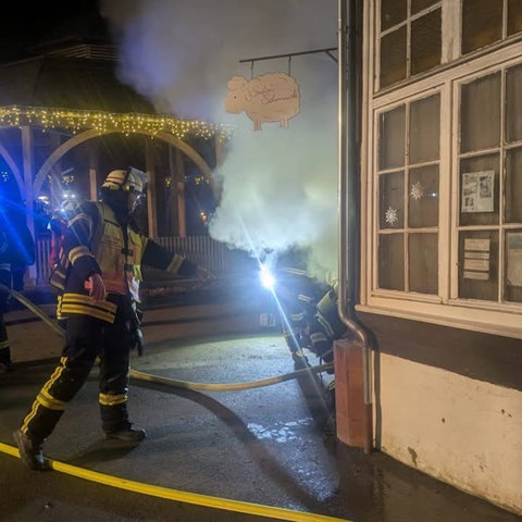 Feuerwehrleute stehen rund um einen kleinen Pavillon, aus dem Rauch drängt