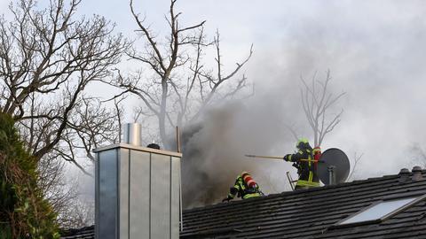 Zwei Feuerwehrmänner auf qualmendem Hausdach