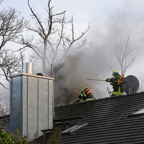 Zwei Feuerwehrmänner auf qualmendem Hausdach