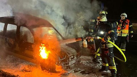 Feuerwehrleute löschen brennenden Pkw, nachts