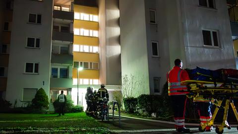 Feuerwehrleute und ein Rettungssanitäter mit Trage im Dunkeln vor einem Haus mit mehreren Parteien