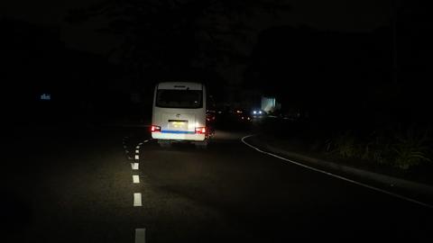 Ein silberner Bus steht mitten in der Nacht auf einer Straße im Dunkeln, nur seine Rücklichter leuchten