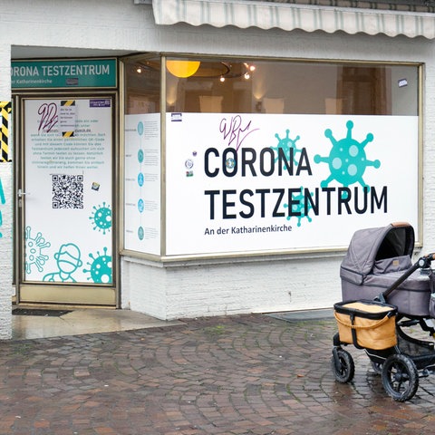 Eine Frau mit Kinderwagen steht vor einem Corona-Testzentrum.