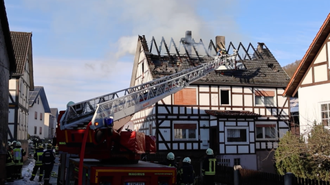 Fachwerkhaus mit ausgebranntem Dach, davor Einsatzfahrzeug der Feuerwehr.