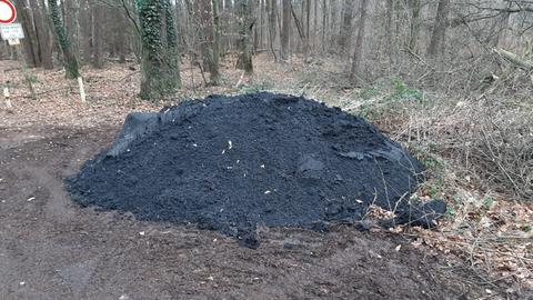 Haufen dunklen Asphalts auf dem Erdboden am Waldrand