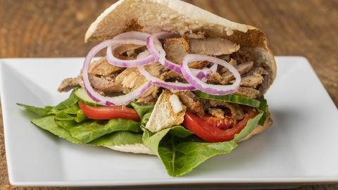 Ein Döner mit Zwiebeln, Tomaten und Salat auf einem weißen eckigen Teller auf Holzgrund.