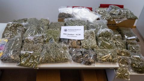 Abgepackt in Tüten liegen rund 20-30 Kilo Drogen auf einem Tisch, hauptsächlich Marihuana. Darauf liegt ein Zettel mit Aufschrift "Polizei Mittelhessen - Rauschgiftdelikte"