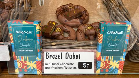 Zwei Dubai-Schokoladen vor einer Korb-Auslage mit Schokolade überzogenen "Dubai-Brezeln" auf dem Frankfurter Weihnachtsmarkt