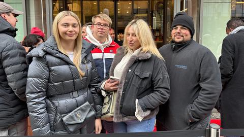 Vor einem Geschäft stehen vier Menschen in einer Warteschlange und lächeln.