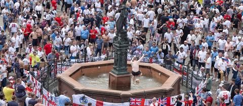 Englische Fans feiern auf dem Römerberg, ein oberkörperfreier Mann spielt mit einem Ball im Justitia-Brunnen.
