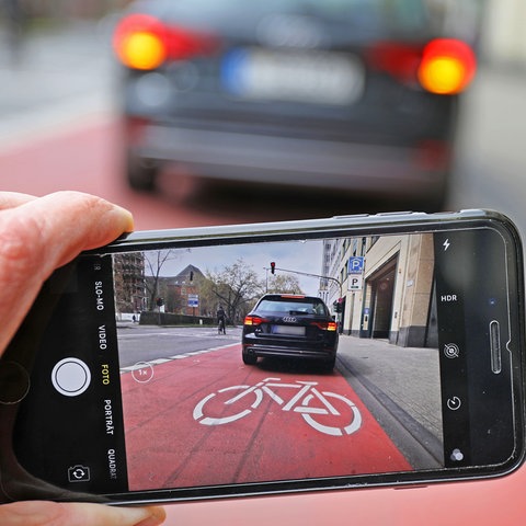 Auf einem Smartphone ist das Bild eines Autos zu sehen, das auf einem Radstreifen hält