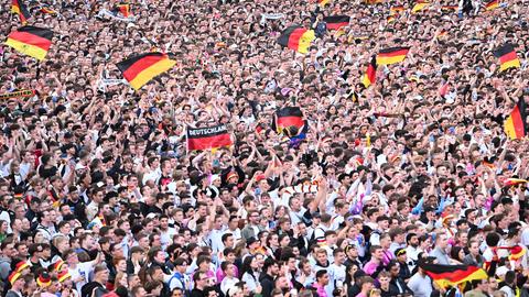 Hunderte Fußballfans stehen dicht gedrängt und schwenken Deutschlandfahnen. Das Bild ist aus der Luft aufgenommen. 