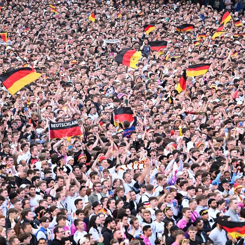 Hunderte Fußballfans stehen dicht gedrängt und schwenken Deutschlandfahnen. Das Bild ist aus der Luft aufgenommen. 