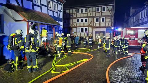 Nachts in Bebra stehen circa 15 Feuerwehrleute vor einem Fachwerkhaus. Flammen sind nicht zu sehen. 