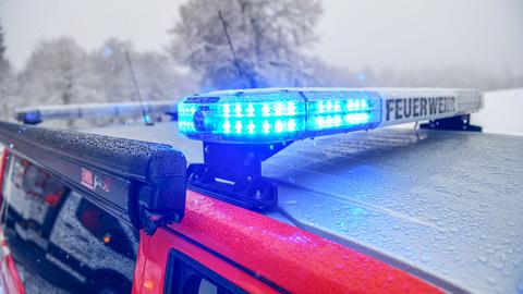 Im Bildvordergrund ein Blaulicht mit Anzeige "Feuerwehr" auf einem Autodach. In Hintergrund - unscharf - eine Winterlandschaft.