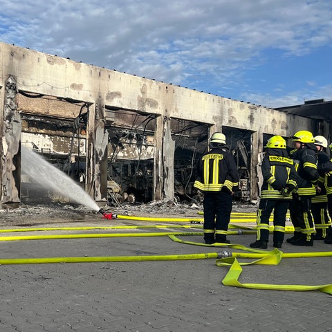 Feuerwehrleute stehen vor dem ausgebrannten Gerätehaus in Stadtallendorf