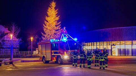 Auf einem Feuerwehrauto steht ein Mann im Weihnachtsmann-Kostüm, mehrere Feuerwehrleute stehen davor.