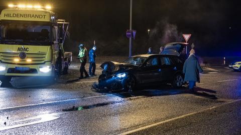 Ein schwarzer Kleinwagen steht mit zerstörter Front auf der Fahrbahn. Ein Aschleppwagen ist zu sehen. 