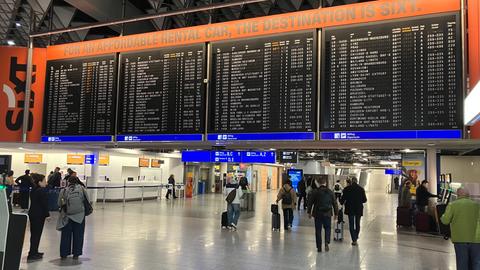 Menschen laufen unter einer Abflugtafelanzeige in einem Terminal in einem Flughafen lang