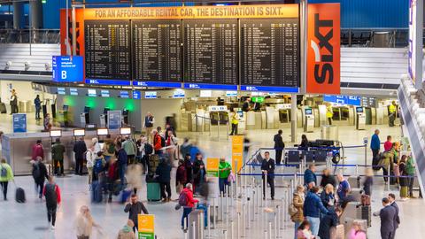 Wartehalle am Flughafen Frankfurt mit vielen Menschen mit Koffern.