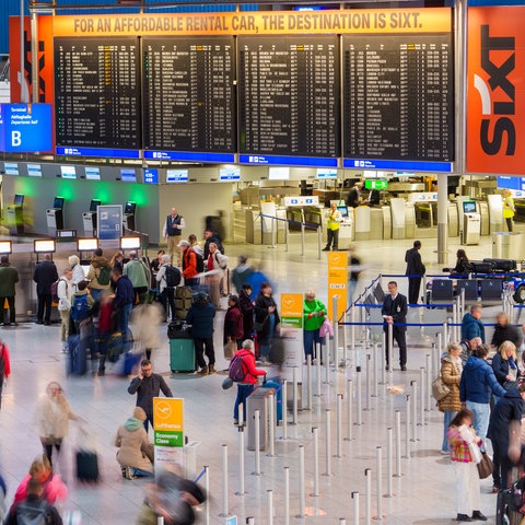 Wartehalle am Flughafen Frankfurt mit vielen Menschen mit Koffern.