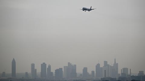 Ein Airbus A321-200 der Lufthansa ist im Landeanflug auf die Nordwest-Landebahn des Flughafens, während die Hochhäuser der Bankenstadt im Dunst liegen.