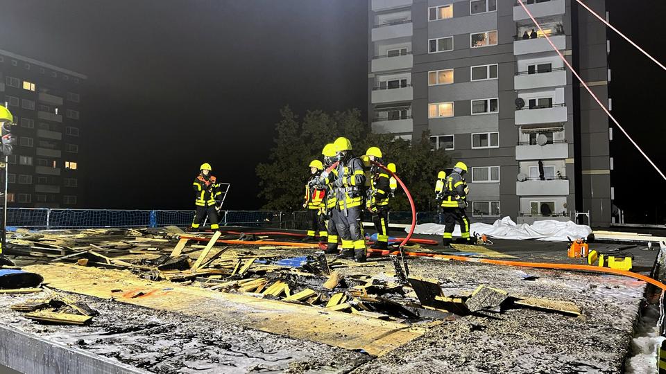 Feuerwehrleute auf einem flachen Dach mit Rußspuren und Resten von Löschschaum