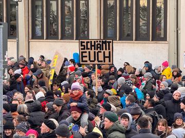 Protestierende Menschen halten Schilder hoch: "Schämt euch" steht auf einem.