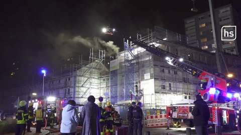 Feuerwehrleute und Bewohner stehen vor einem Haus, aus dem es raucht.